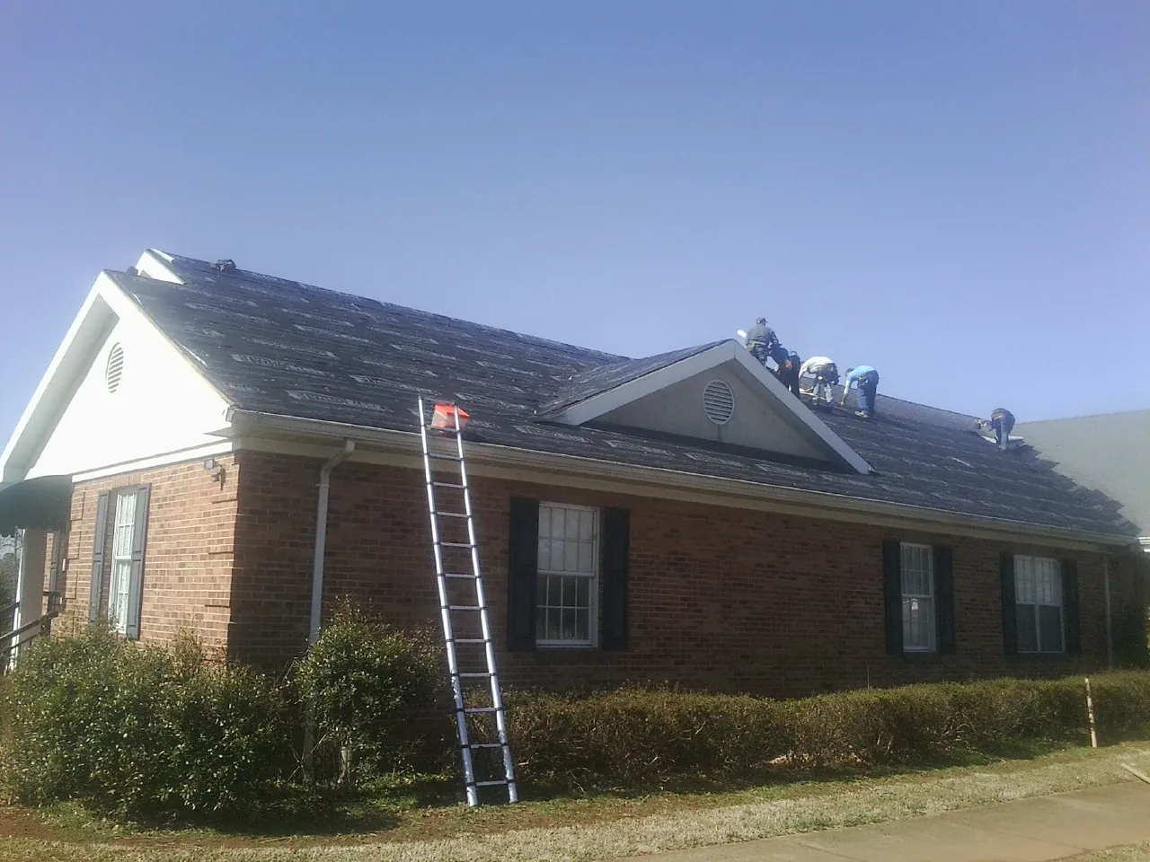Crew tearing shingles off a brick ranch roof with a ladder set — Emergency Roof Repair work by our crew in Yale