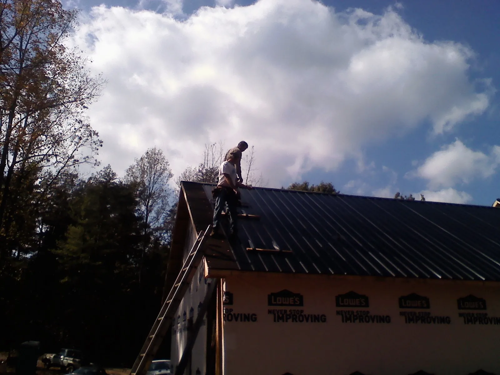Roofer fastening dark metal panels high against a cloudy sky, from a Roof Inspection job in Yale